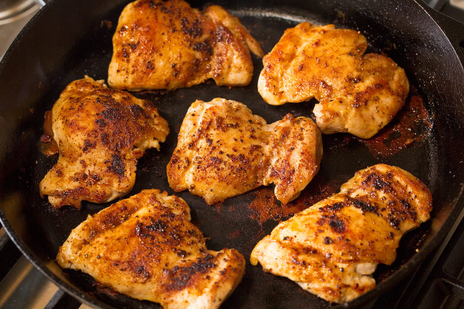 Apple Chicken Chicken thighs shown cooked through in a cast iron pan on second side.