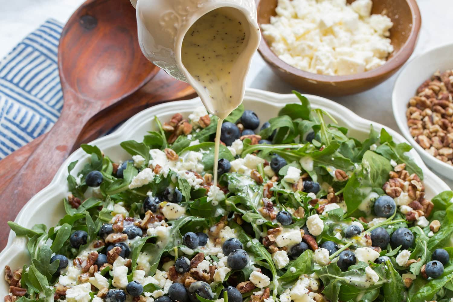 Blueberry Salad Lemon poppy seed dressing being drizzled over blueberry arugula salad.