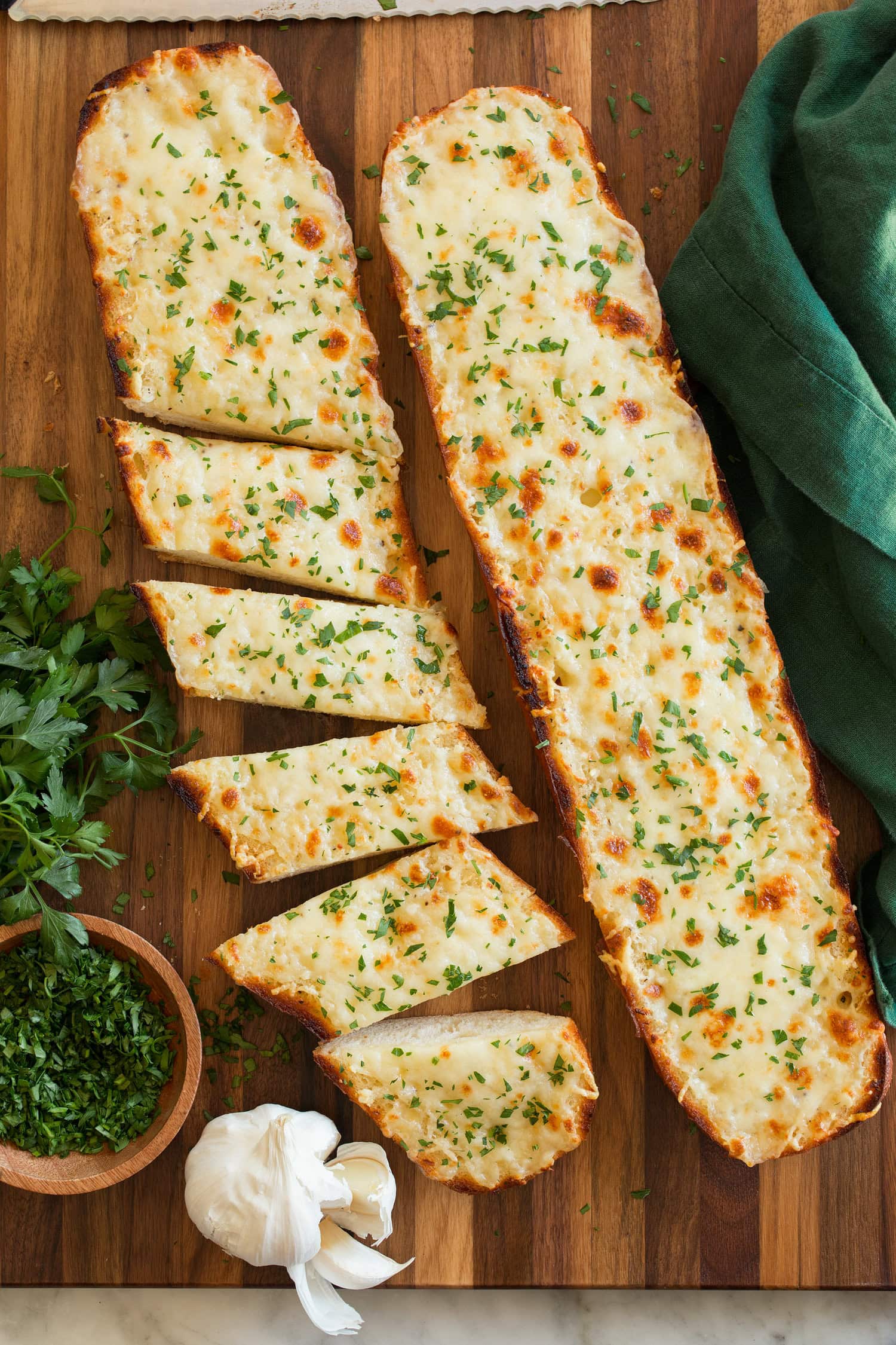 Cheesy Garlic Bread Two halves of cheese garlic bread on a cutting board, one is cut into slices.