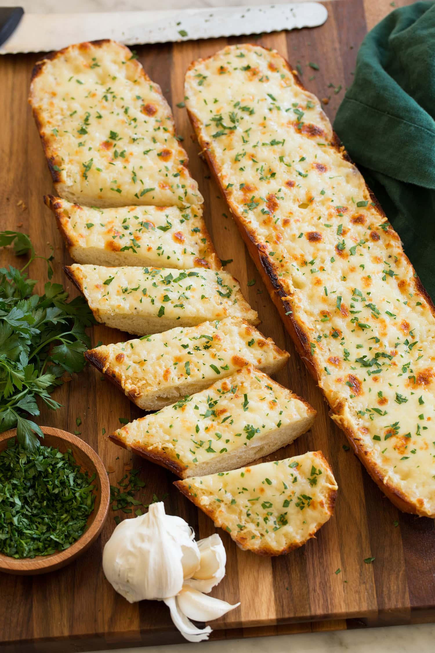 Cheesy Garlic Bread Cheesy garlic bread cut into slices with garlic and parsley shown to the side.