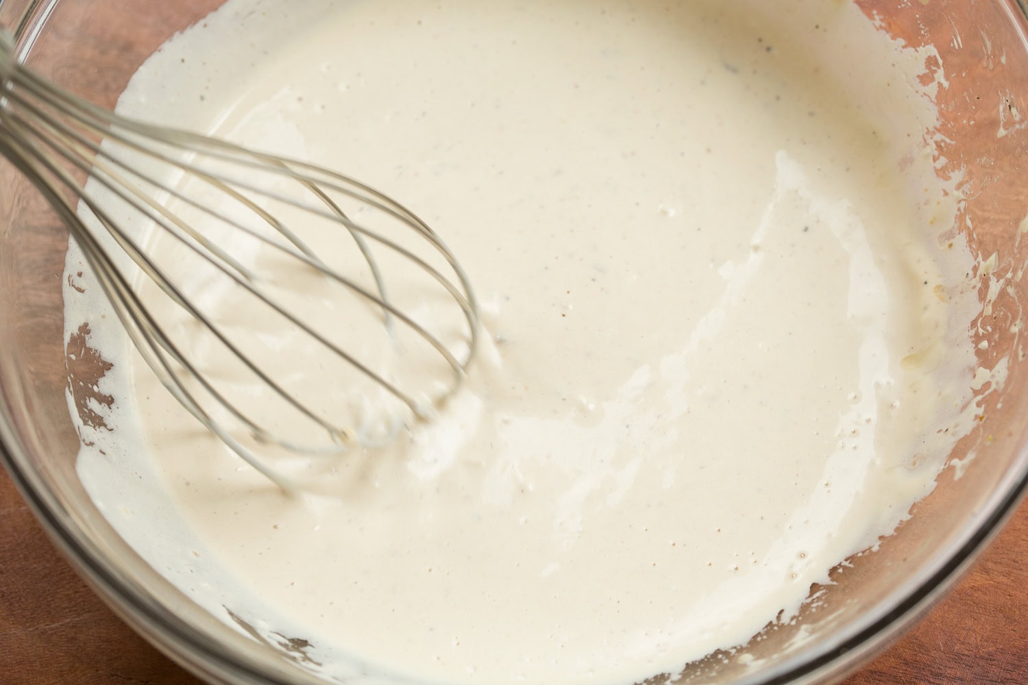 Chicken Caesar Wrap Caesar dressing in glass mixing bowl shown after mixing.