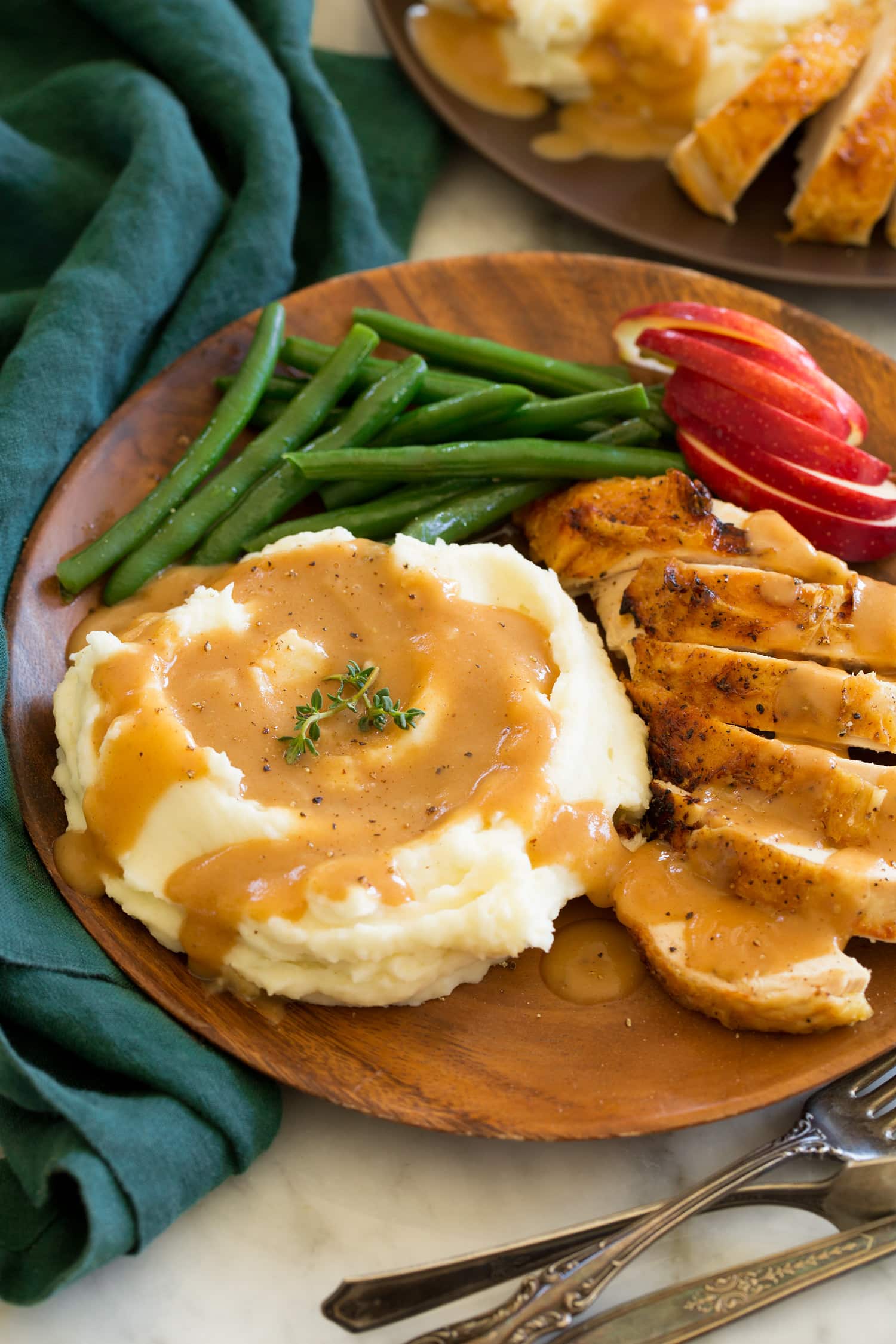 Chicken Gravy Chicken gravy shown on mashed potatoes with a side of roasted chicken, apples and green beans as a serving suggestion.