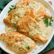 Creamy dijon mustard chicken shown on a white oval serving platter over a green cloth and a wooden tray.