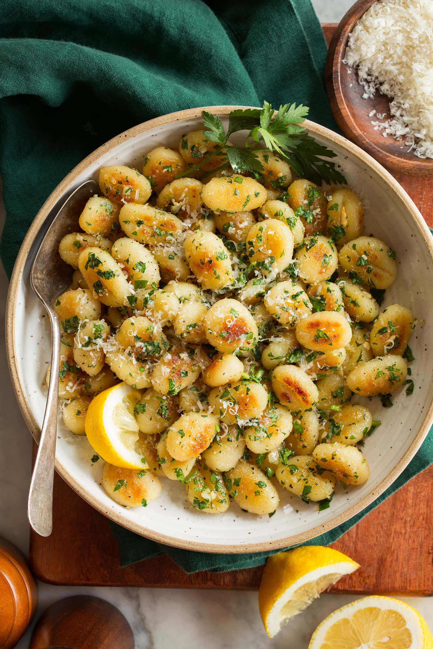 Pan Fried Gnocchi Pan fried gnocchi with lemon wedges, shown in a cream bowl over a wooden surface with a green cloth.