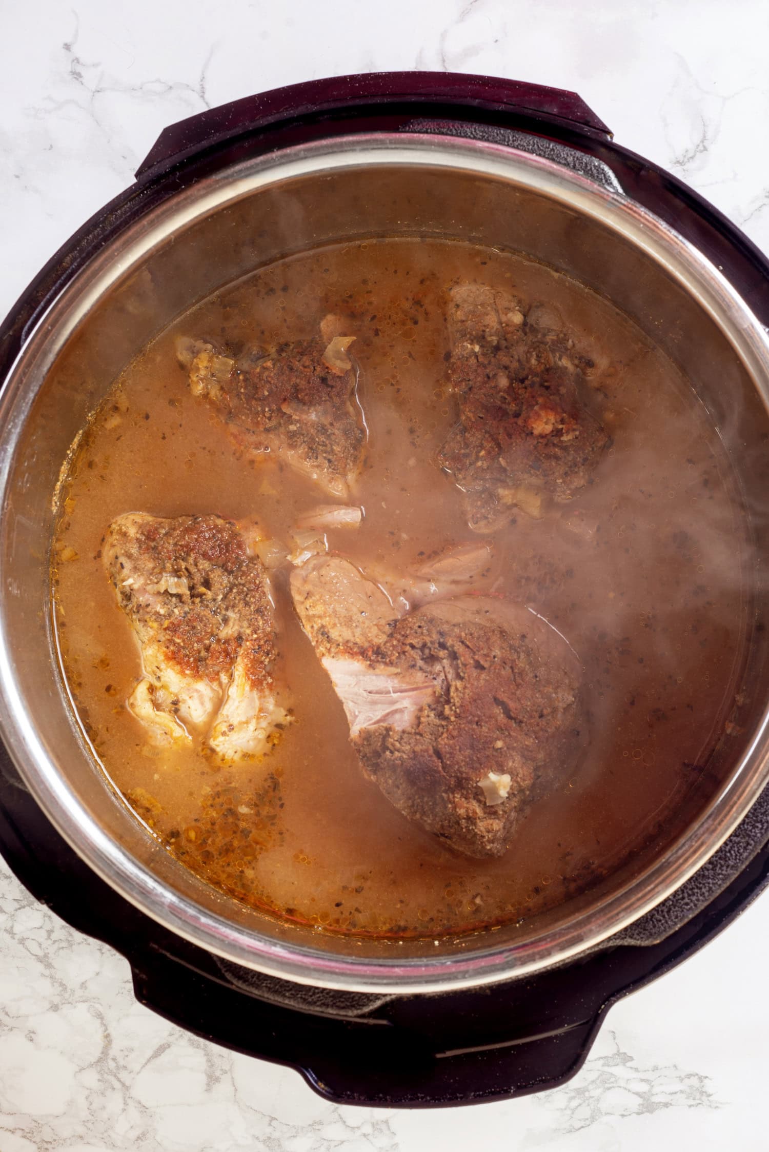 How to Make Carnitas in the Slow Cooker Place pork in slow cooker. Pour in chicken broth, orange juice and lime juice. Sprinkle in salt, pepper, cumin, oregano, coriander, chili powder and cayenne pepper, onions and garlic. Cover and cook on low heat 8 hours. Leave liquid in slow cooker, remove pork and shred with two forks. Spray a rimmed 18 by 13-inch baking sheet with non-stick cooking spray. Place pork on baking sheet, pour over 1 cup reserved broth (try and strain out onions when ladling broth out), drizzle with oil and toss and spread into an even layer. Position oven rack near broiler and preheat broiler to high. Broil until pork is browned and crispy in places about 3 - 6 minutes. Serve warm in tortillas with desired toppings. Carnitas finished cooking, shown steaming in the cooking broth.