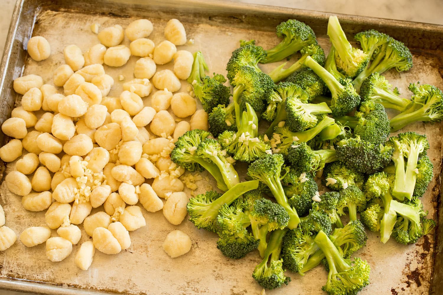 Sheet Pan Gnocchi with Sausage and Broccoli Broccoli, gnocchi, garlic and olive oil on sheet pan before tossing.