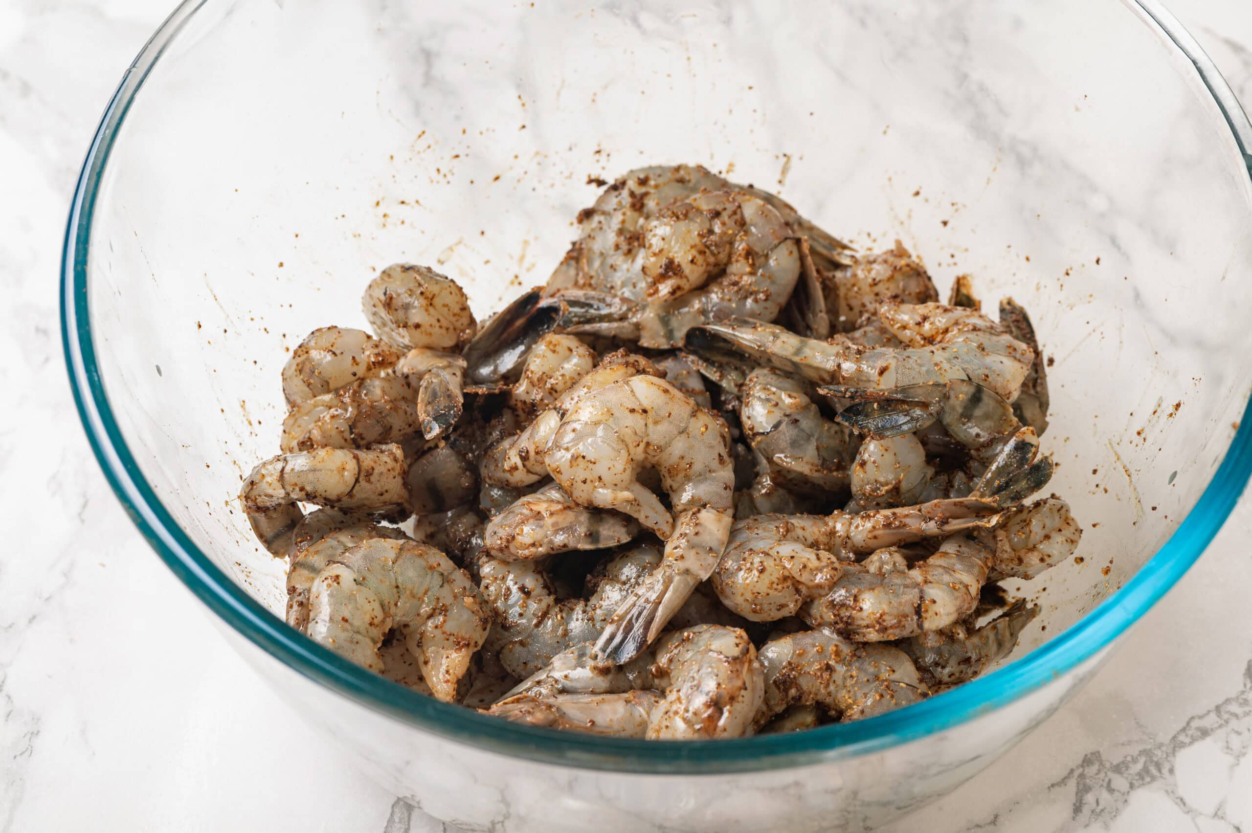 Shrimp Fajitas Tossing raw shrimp with Mexican spices in a glass bowl.