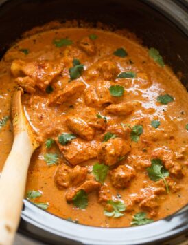 Slow cooker chicken tikka masala garnished with cilantro in a black crockpot.