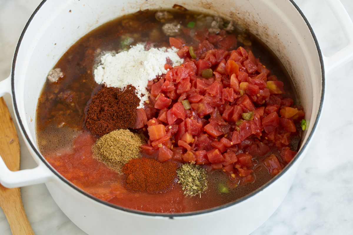 Taco Soup - easy, incredibly tasty soup! Loaded with hearty ingredients and brimming with delicious seasoned flavor. Perfect for cold fall and winter days! #tacosoup #soup #fall #recipe Adding tomatoes and spices to pot to make taco soup.