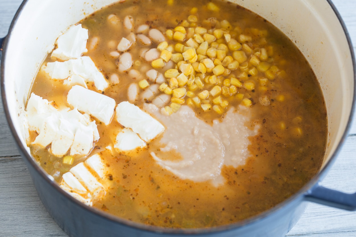 White Chicken Chili Adding cream cheese, corn and pureed bean mixture to white chicken chili mixture in pot.